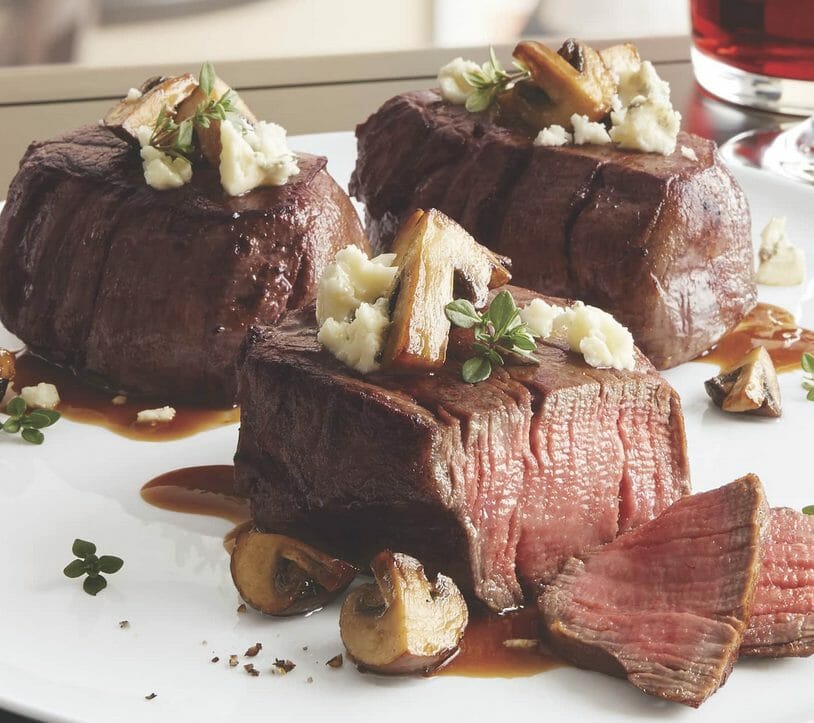 Three Black Angus filets on a white serving platter with a mushroom and blue cheese garnish and sauce.