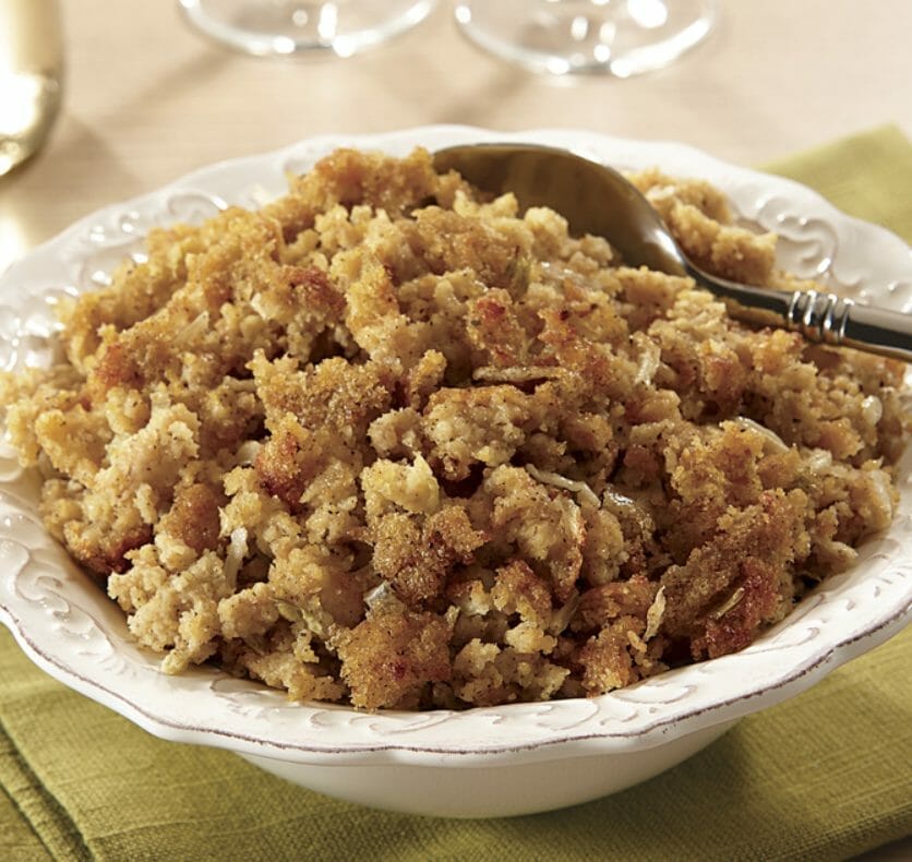 Cornbread dressing in a white bowl with decorative rim and a serving spoon.
