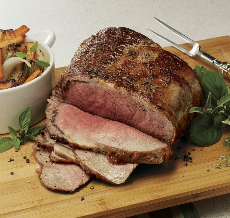 Medium-rare Prime Rib from a roasting bag, sliced on a wooden serving tray, with roasted vegetables on the side.