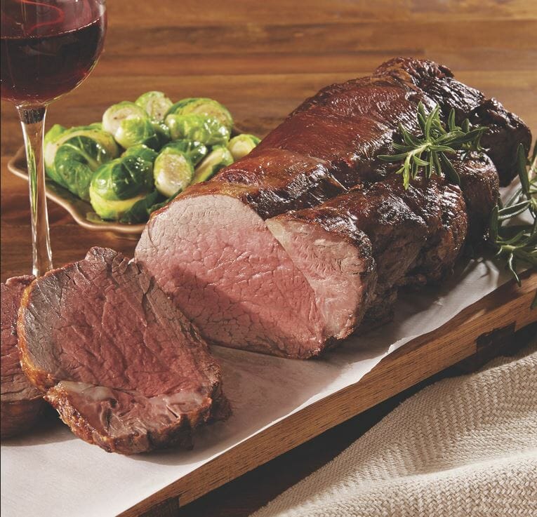 Medium-rare Tenderloin for Chateaubriand on a wooden serving tray, with brussel sprouts and a glass of wine.