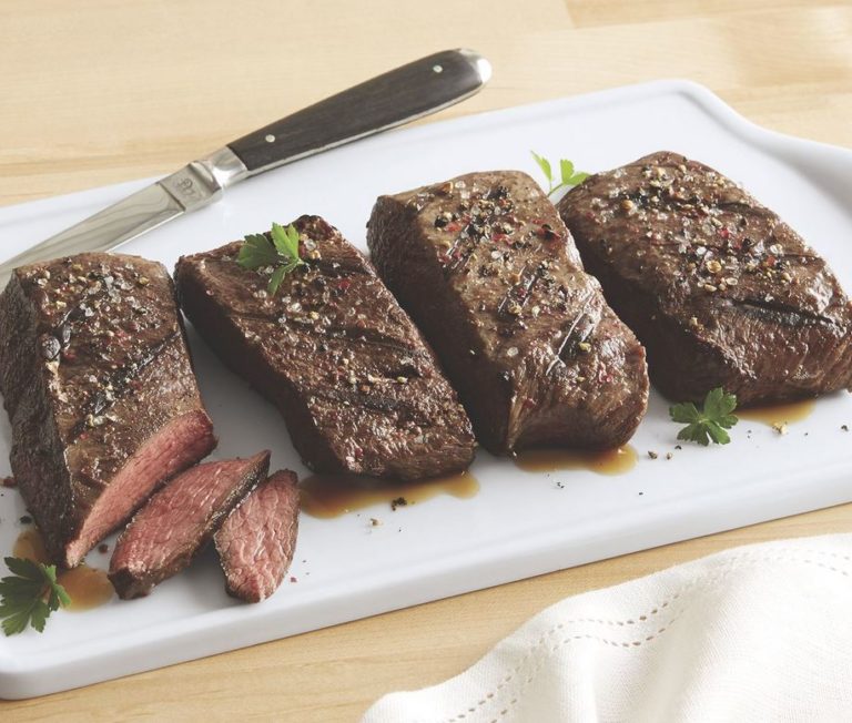 Four selections of seasoned, grilled Black Angus steak on a white serving platter with a steak knife.