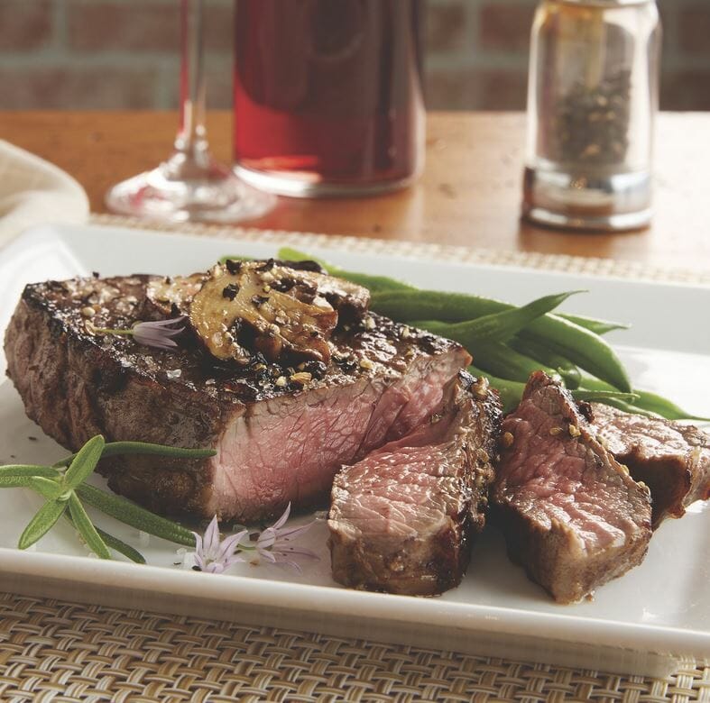 Seasoned medium-rare Black Angus sirloin steak with sauteed mushrooms and green beans on a white plate.