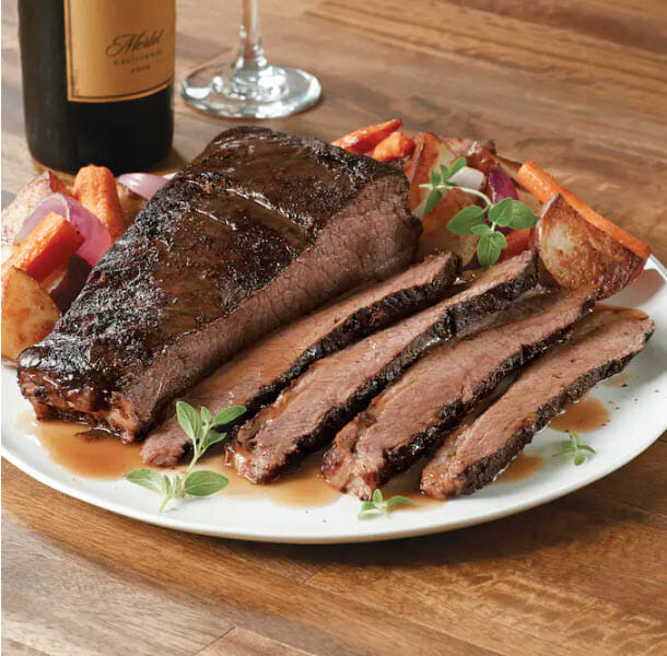 Sliced cooked brisket on a white plate with vegetables
