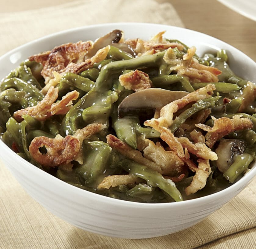 Green bean casserole with mushrooms, crispy onions and sauce in a white bowl.