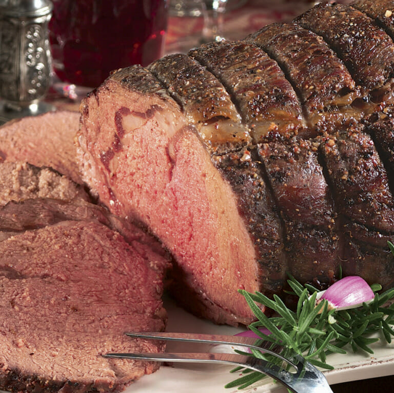 A seasoned medium-rare Prime Rib Roast with rosemary garnish, sliced and ready to serve with a meat fork.