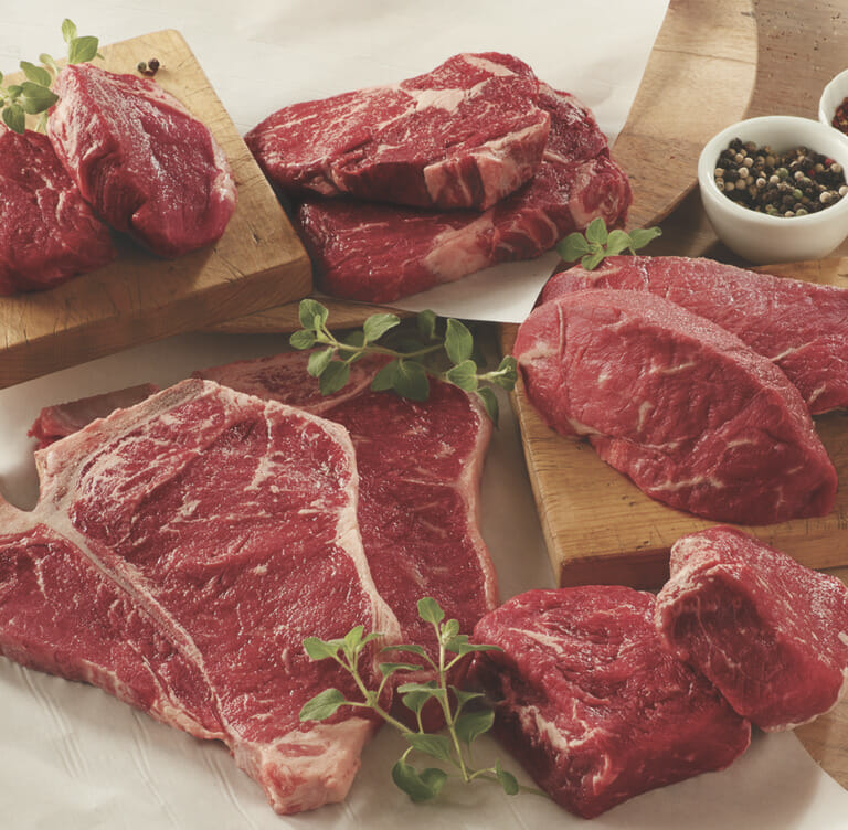 A steak sampler including two each of five different cuts displayed on wooden boards, with peppercorns and garnish.