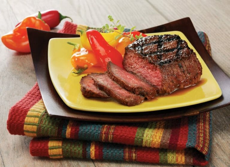 Sliced medium-rare Chipotle flavored sirloin steak, red and yellow peppers on the yellow plate, and colorful placemat.