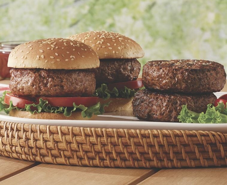 A basketed platter of thick, juicy grass fed burgers, two on seeded buns with lettuce and tomato slices.