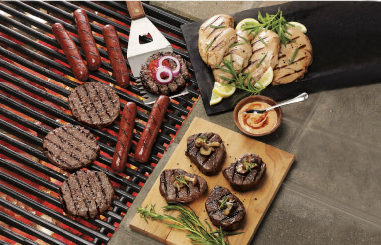 Favorite meats just off a hot grill, including burgers, steaks, chicken breasts, and franks with sauce and garnish.