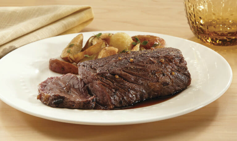 Marinated Hanger steak with roasted potato wedges on a white plate.