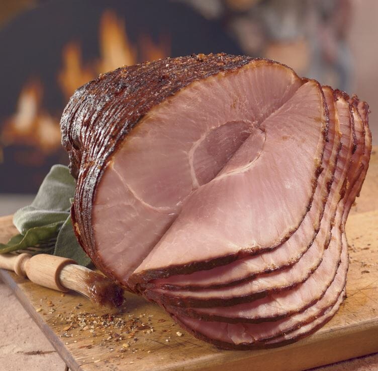 Our Honey Glazed Spiral Sliced Ham with seasonings on a wooden cutting board.