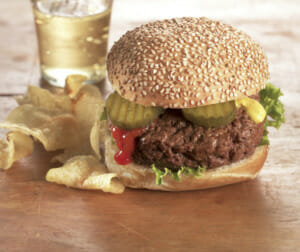A juicy sirloin steak burger on a seeded bun with lettuce, pickle, ketchup and mustard and a side of potato chips.