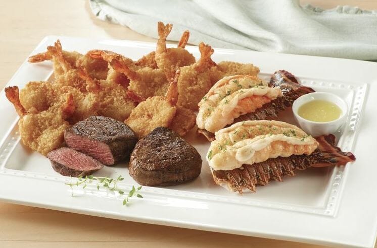 A white platter of breaded shrimp, two steak filets, two lobster tails, and melted butter for dipping.