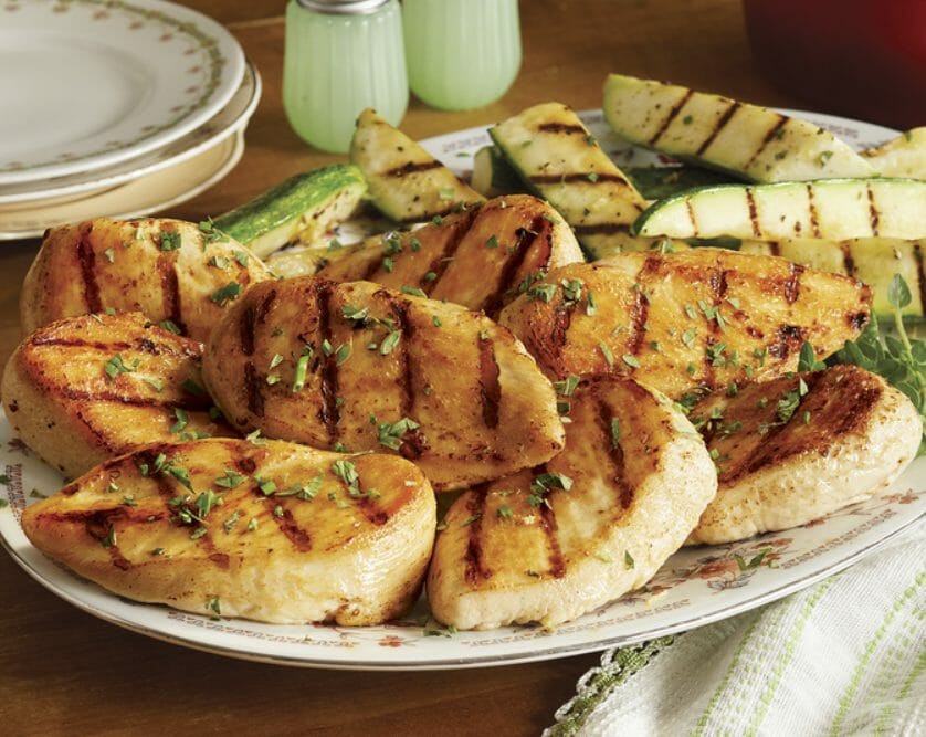 Tasty grilled chicken breasts with an herbal garnish on a platter accompanied by grilled zucchini squash wedges.