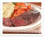 Seasoned, grilled steak on a plate with mashed potatoes and garnished carrot slices.