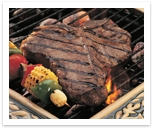 Grilled Porterhouse steak next to a vegetable shishkabob over a flaming grill.