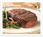 Seasoned, grilled sirloin steak on a white plate with green beans and sweet pepper bits.